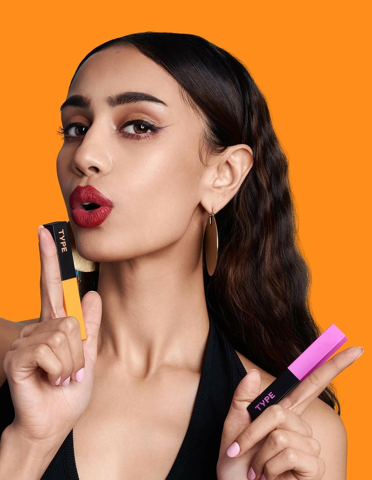 Model showcasing LIGHT UP LIPSTICK in vibrant colors against orange background.